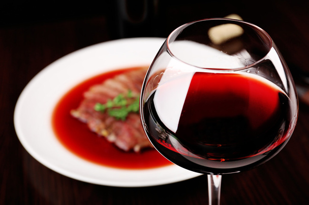 Склянка вина з смаженим стейком у винному соусі на темному фоні
 - Фото, зображення