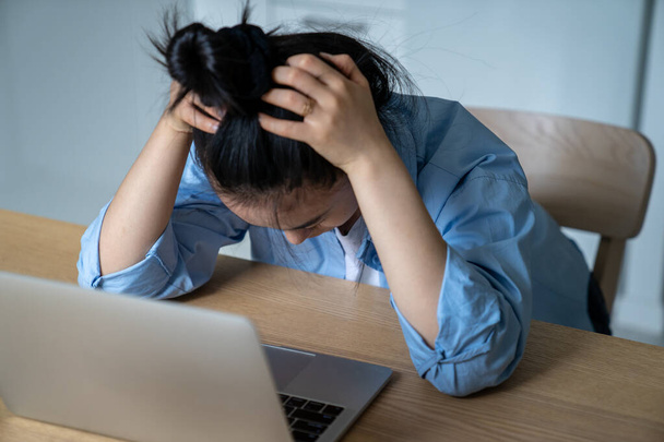 Sfrustrowana młoda kobieta przedsiębiorca e-commerce siedzi przy biurku z laptopem trzymając głowę w dłoniach, mając problemy biznesowe online, selektywne skupienie. Praca na własny rachunek i zdrowie psychiczne - Zdjęcie, obraz