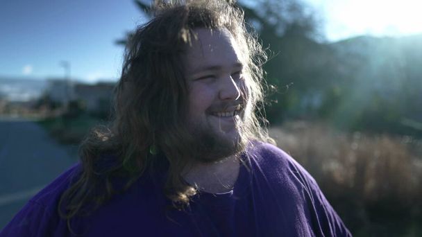 Funny Young happy man takes off the rubber band from his hair outside. An overweight person feeling free shaking head with long hair - Photo, image