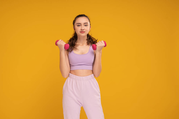 Young fitness woman in fashionable sporty clothes posing on the yellow studio background. A lo of copy space. Healthy lifestyle concept. Beautiful active student girl. - Fotó, kép
