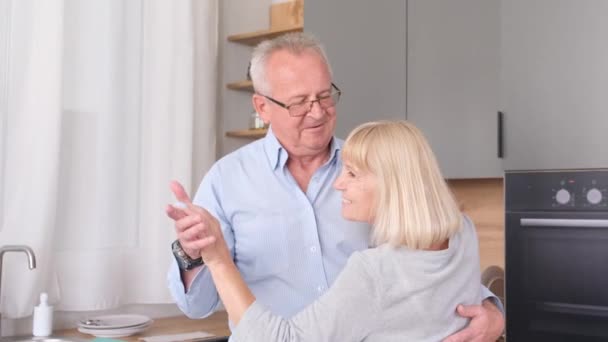 Happy old mature man and woman having fun, having fun together indoors, doing fun household chores. Senior couple dancing together in the kitchen, smiling. - Imágenes, Vídeo
