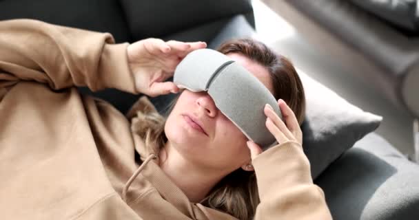 Jeune femme couchée sur le canapé et mettant des lunettes de massage sur ses yeux film 4k au ralenti. Style de vie sain concept de fatigue oculaire - Séquence, vidéo