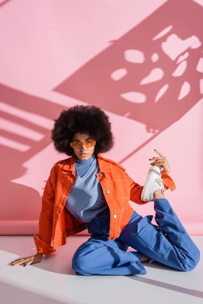full length of young african american woman in stylish orange sunglasses and trendy outfit posing on pink  - Fotografie, Obrázek