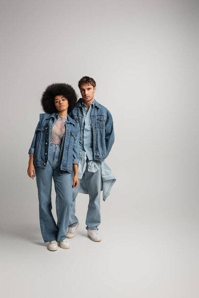 full length of young interracial man and woman standing in total denim outfit on grey  - Photo, Image