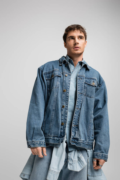 young man in denim jacket posing and looking away isolated on grey  - Foto, Imagem