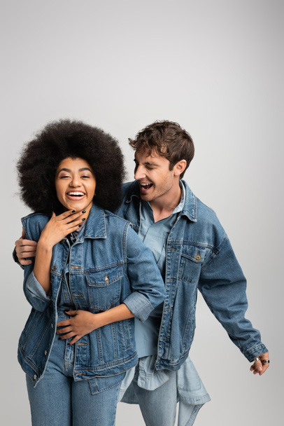 happy multiethnic man and woman in denim outfit laughing isolated on grey  - Fotoğraf, Görsel