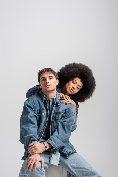 curly african american model looking at camera with stylish man sitting isolated on grey  - Photo, image