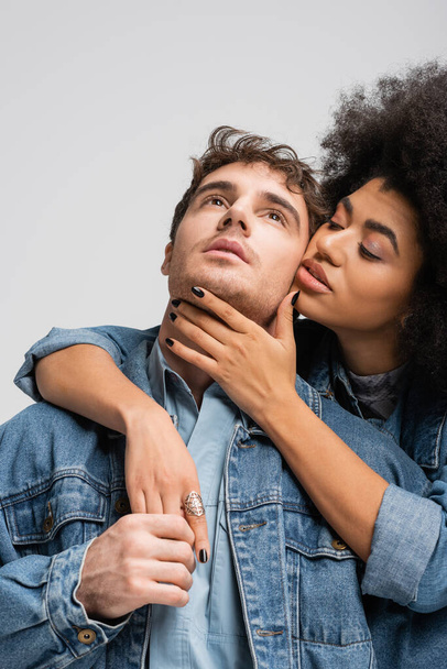 curly african american model embracing stylish man in denim clothes isolated on grey  - Valokuva, kuva