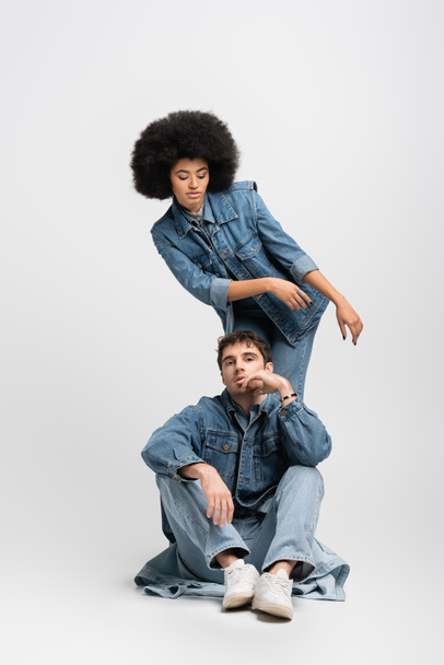 full length of curly african american woman standing behind man in denim outfit and sneakers on grey - Fotó, kép