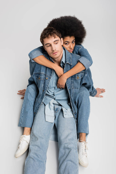 high angle view of stylish african american woman sitting and hugging stylish man in denim clothes on grey  - Foto, Imagem