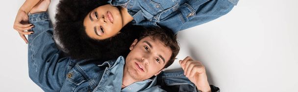 top view of stylish interracial couple in denim clothes lying on grey background, banner  - Foto, Imagen