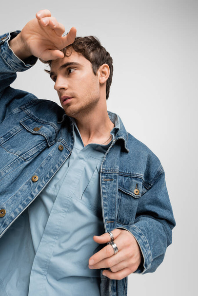 stylish young man in denim clothes posing and looking away isolated on grey  - Foto, immagini