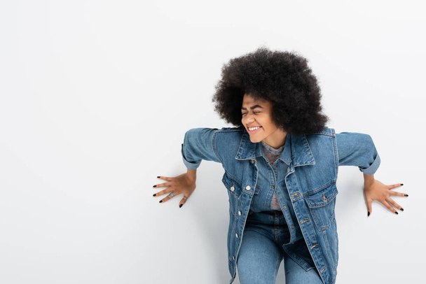 curly african american woman in denim jacket smiling with closed eyes against grey wall  - Foto, Bild