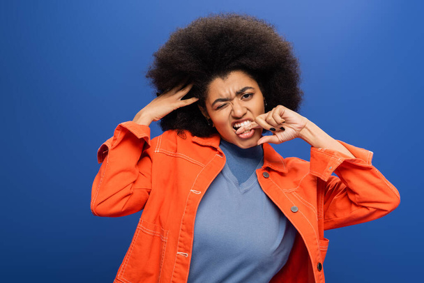 Stylish african american woman winking and biting finger isolated on blue  - Foto, Imagem