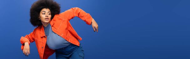 Trendy african american woman in orange jacket posing on blue background, banner  - Foto, immagini