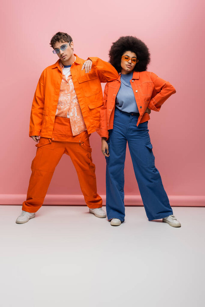 Fashionable multiethnic couple in sunglasses posing on pink background  - Zdjęcie, obraz