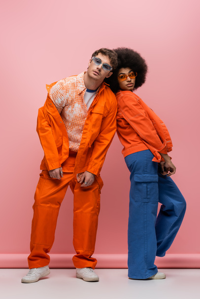 Stylish interracial couple in jackets looking at camera on pink background  - Fotó, kép