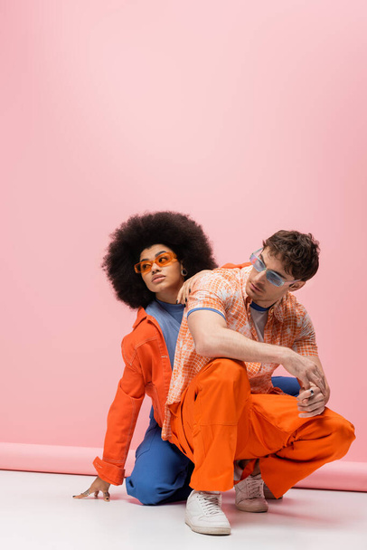 Trendy man in sunglasses posing near african american woman on pink background  - Φωτογραφία, εικόνα