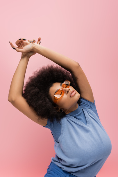 Young african american woman in sunglasses and blue vest posing isolated on pink  - Φωτογραφία, εικόνα