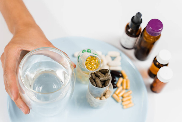 Многие пищевые добавки таблетки и стакан воды для ежедневного приема таблеток на белом фоне. Комплект мультивитаминов, аминокислот, минералов и магния антистресс, мелатонин крупным планом - Фото, изображение