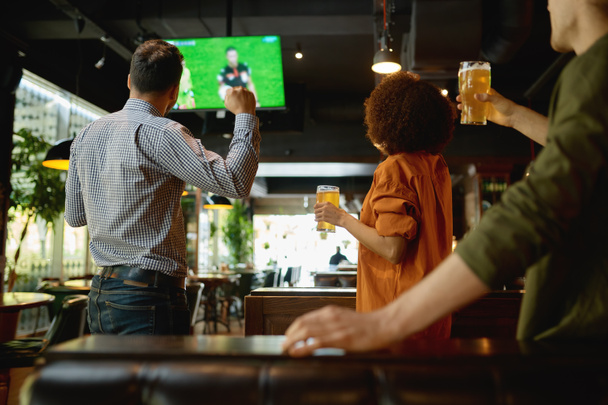 Bir grup arkadaş televizyon ekranında maç izleyip bira içiyorlar. Gençler spor barında ya da barda dinleniyor - Fotoğraf, Görsel