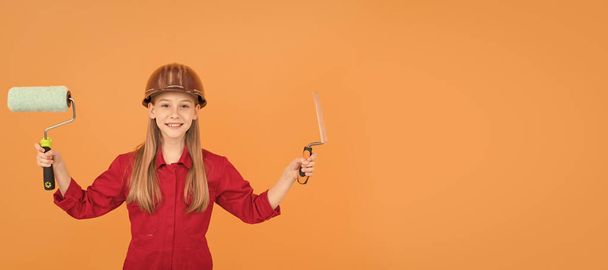 happy teen child in builder hard hat with paint roller and spatula on orange wall. - Фото, изображение