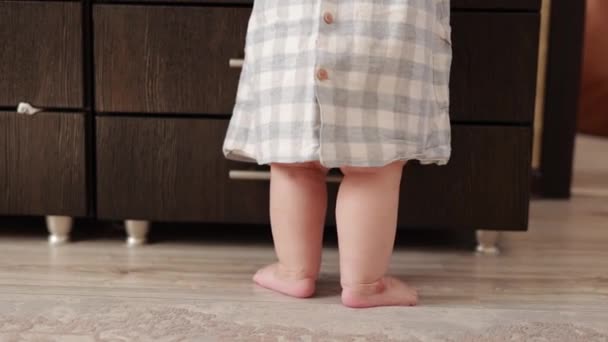 Baby first steps. Little infant feet standing, moving, dancing and walking on floor, close-up. Baby learning to walk at home. Toddler exploring home, concept newborn and childhood, slow motion - Felvétel, videó