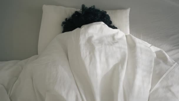 Farbige Frau, die in die strahlende Sonne blickt und die Augen schließt und sich unter einer Decke versteckt. Afroamerikanerin wacht am frühen Morgen im Bett auf und fühlt sich müde nach schlafloser Nacht, Schlafmangel und Faulheit - Filmmaterial, Video