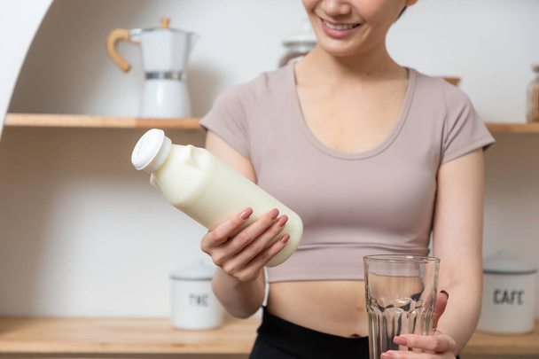 Здоровая молодая азиатка выбирает молоко с кальцием для крепких костей дома. Велнес со здоровой концепцией - Фото, изображение