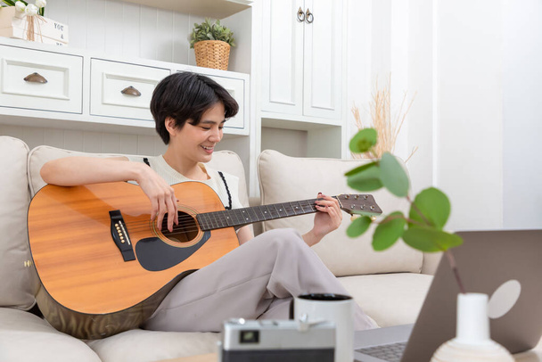 Playful asian woman playing acoustic guitar music instrument at home, young Asian musician girl lifestyle - Photo, Image