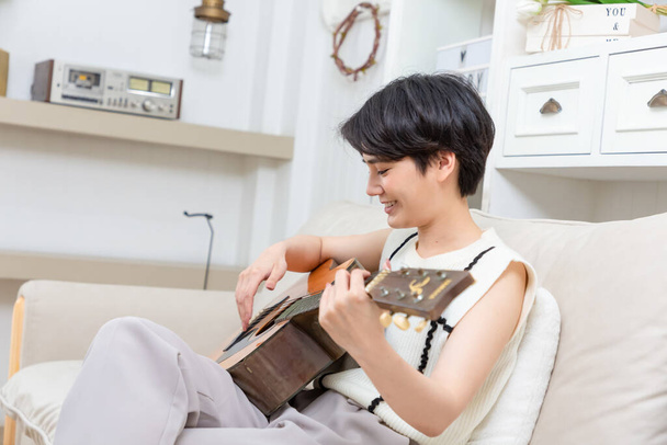 Playful asian woman playing acoustic guitar music instrument at home, young Asian musician girl lifestyle - Photo, image