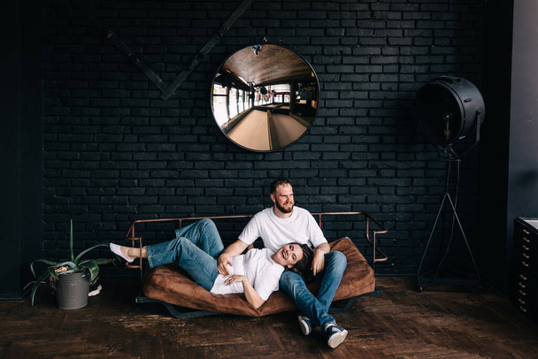 Портрет влюбленной пары, сидящей на диване в современных квартирах-студиях, концепция захвата счастливого момента, гармоничные отношения, забота и искренние чувства - Фото, изображение