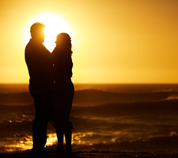 Silhouette of mature couple hugging at sunset. Senior couple being affectionate on the beach. Mature couple embracing on holiday on the beach. Married couple bonding on the beach at sunset. - Photo, image