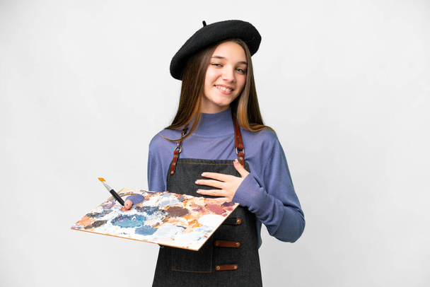 Молодой художник держит палитру на изолированном белом фоне, много улыбаясь - Фото, изображение