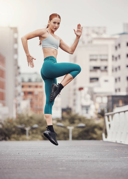 Warm up, jump and health with woman in city for training, fitness and cardio endurance. Energy, workout and exercise with girl athlete jumping in urban town for sports, running and body wellness. - Photo, image