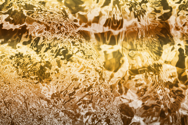 Размытый прозрачный желто-золотой цвет прозрачной спокойной текстуры поверхности воды с шипами и пузырями. Модный абстрактный фон природы. Водные волны в солнечном свете. водный фон, масло - Фото, изображение