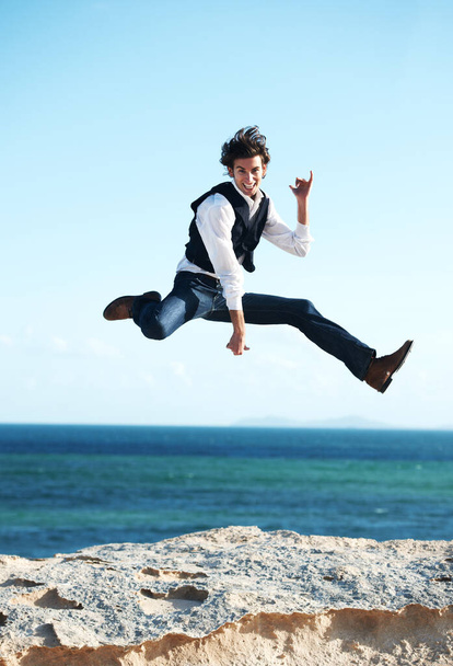 What a great feeling. Happy young man jumping in the air with the ocean in the background - 写真・画像