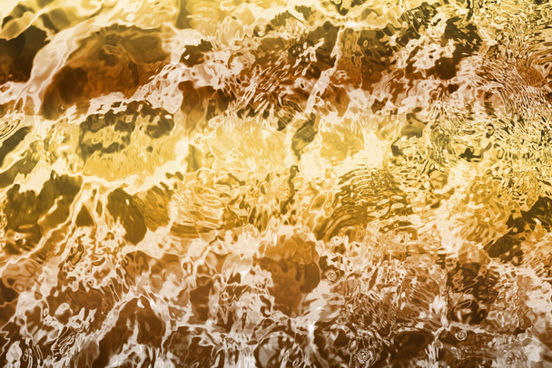 Размытый прозрачный желто-золотой цвет прозрачной спокойной текстуры поверхности воды с шипами и пузырями. Модный абстрактный фон природы. Водные волны в солнечном свете. водный фон, масло - Фото, изображение