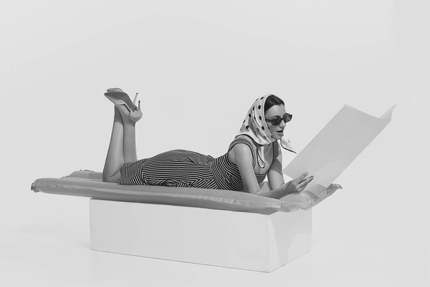 Nyári szünet. Egy monokróm portré fiatal, gyönyörű nőről, aki felfújható matracon fekszik és magazint olvas. Retro vintage stílus, 70-es, 80-as évek divat. Reklámhely másolása - Fotó, kép