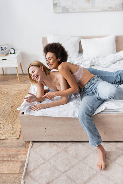 hoge hoek uitzicht van jonge interraciale vrouwen in jeans en lingerie plezier hebben op bed thuis - Foto, afbeelding