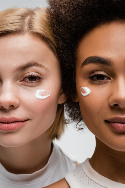 Nahaufnahme von jungen interrassischen Frauen mit Gesichtscremeabstrichen isoliert auf grau - Foto, Bild