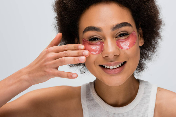 happy african american model applying collagen eye patches while looking at camera isolated on grey - Foto, imagen