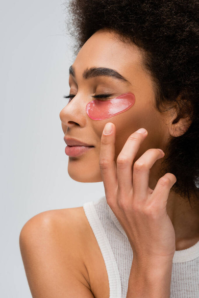 young african american model with closed eyes and collagen eye patches holding hand near face isolated on grey - Photo, Image
