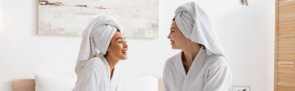 mujeres muy multiétnicas en albornoces de felpa y toallas sonriéndose en el dormitorio, pancarta - Foto, imagen