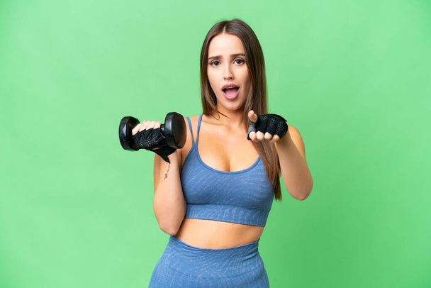 Young sport woman making weightlifting over isolated chroma key background surprised and pointing front - Fotografie, Obrázek