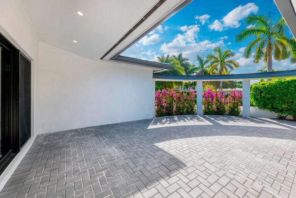 Hermoso patio trasero de elegante casa moderna en el barrio Nautilius de Miami Beach, muro de flores, piso de cemento, columnas, árboles tropicales y plantas, cielo azul en el fondo - Foto, Imagen