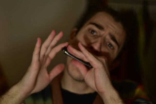 White Caucasian male playing harmonica at home passionately  - Foto, afbeelding