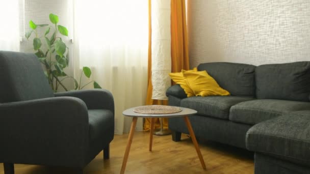 Άνετο σαλόνι διαμέρισμα με καναπέ και κίτρινα μαξιλάρια και κομψό τραπέζι, παράθυρο με φωτεινό φως ημέρας έξω το χειμώνα - Πλάνα, βίντεο