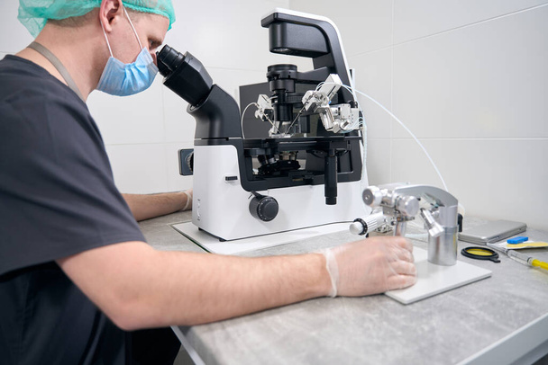 Embryologe hinter dem Verfahren der Befruchtung der Eizelle, der Mann verwendet moderne Geräte - Foto, Bild