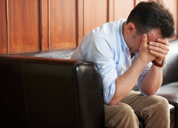 Stricken with grief. a grief-stricken man sitting on a sofa with his head in his hands - Foto, Bild